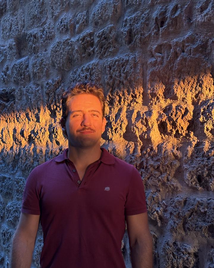 Gabriele Lippi in a burgundy polo shirt, against an old stone wall lit by a band of low evening sun.